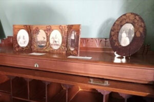 This is a photo of a few photo frames memorabilia on top of a wooden cabinet at La Maison Macdonell-Williamson House