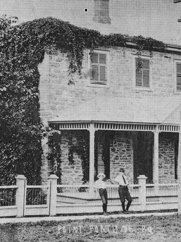 This is an old photo or postcard of La Maison Macdonell-Williamson House with two young boys leaning on the front fence.